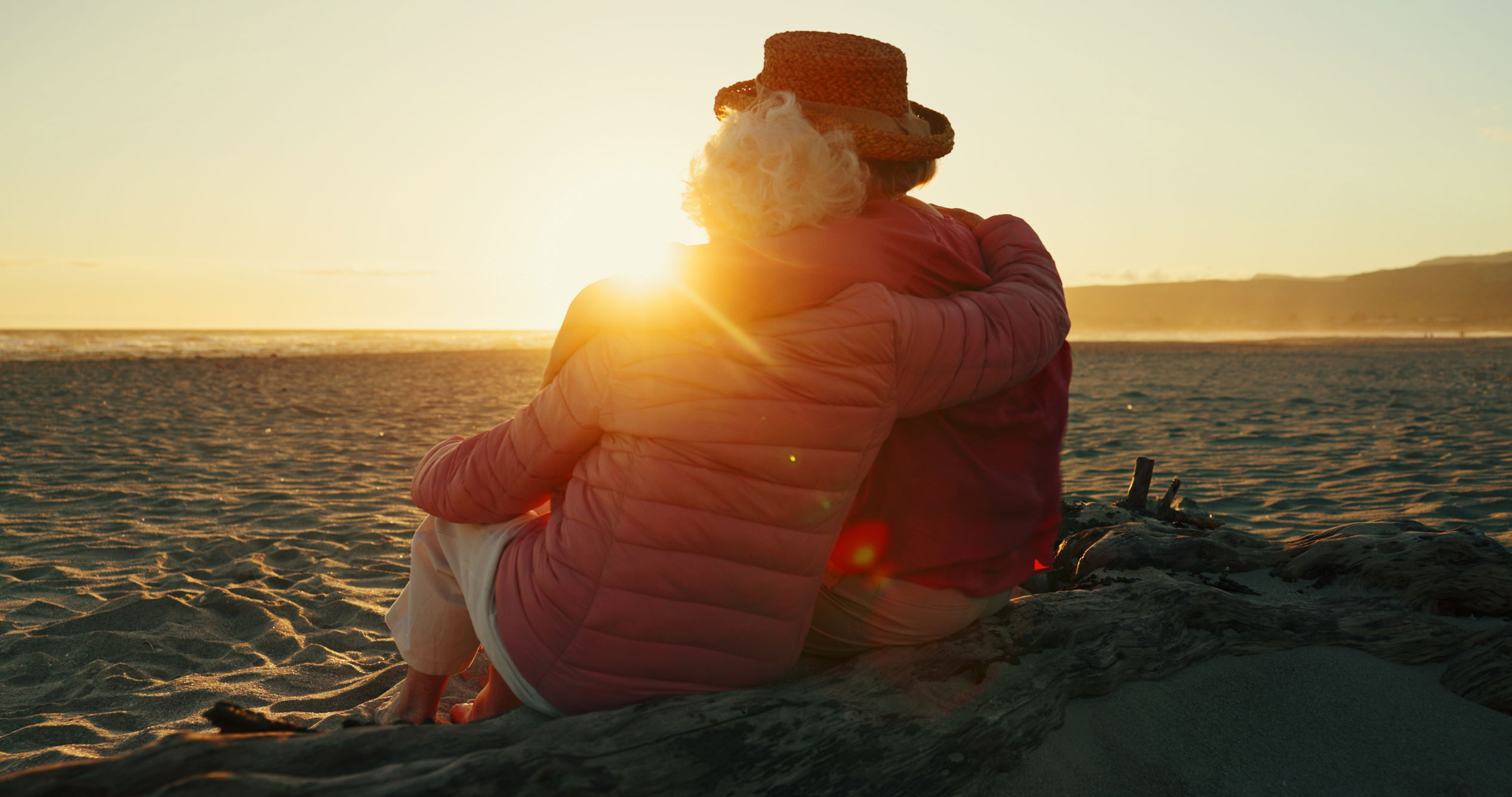 Ældre par holder om hinanden og kigger ud over havet i solnedgang